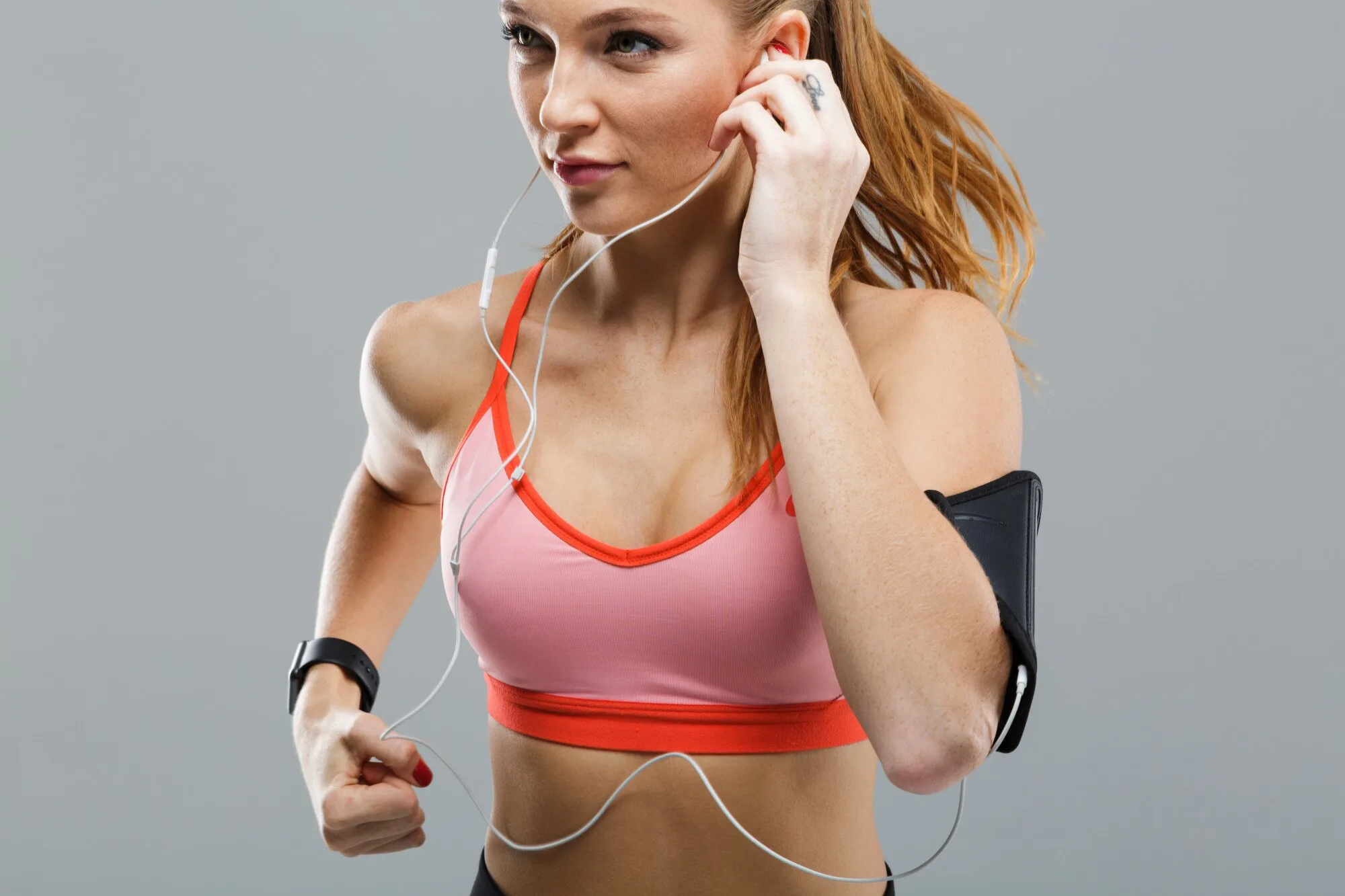 Mulher ruiva correndo ajustando fone de ouvido, bela mulher ruiva fitness de top rosa, corrida, melhor fone de ouvido para corrida, top rosa, fio do fone sobre seio, look fitness