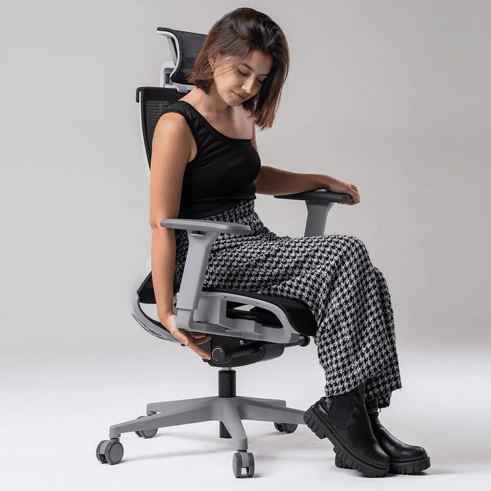 Garota bela e jovem com blusa de alça única e calça xadrez sentada na cadeira ergonômica Elements Vertta, ajustando o assento
