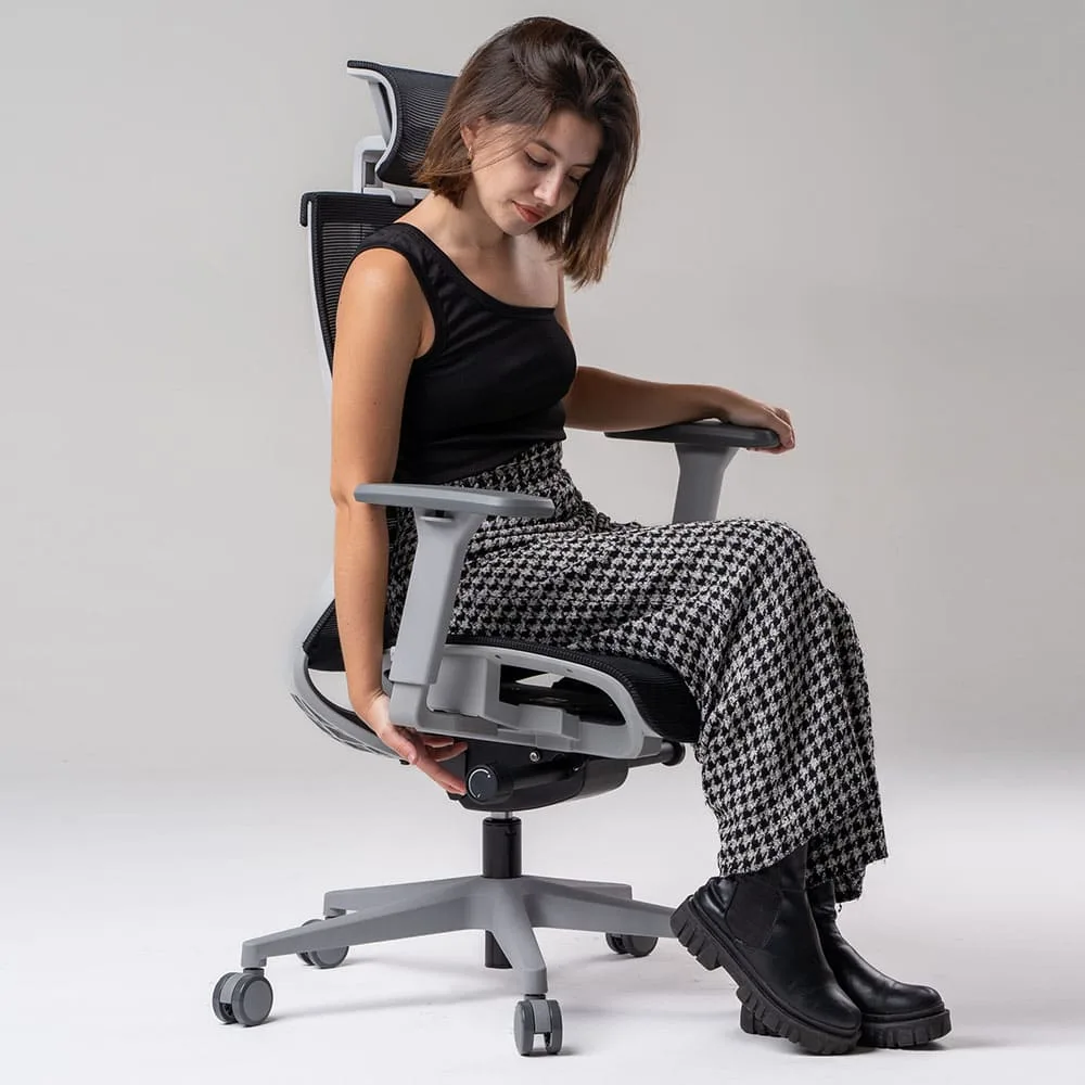 Garota bela e jovem com blusa de alça única e calça xadrez sentada na cadeira ergonômica Elements Vertta, ajustando o assento