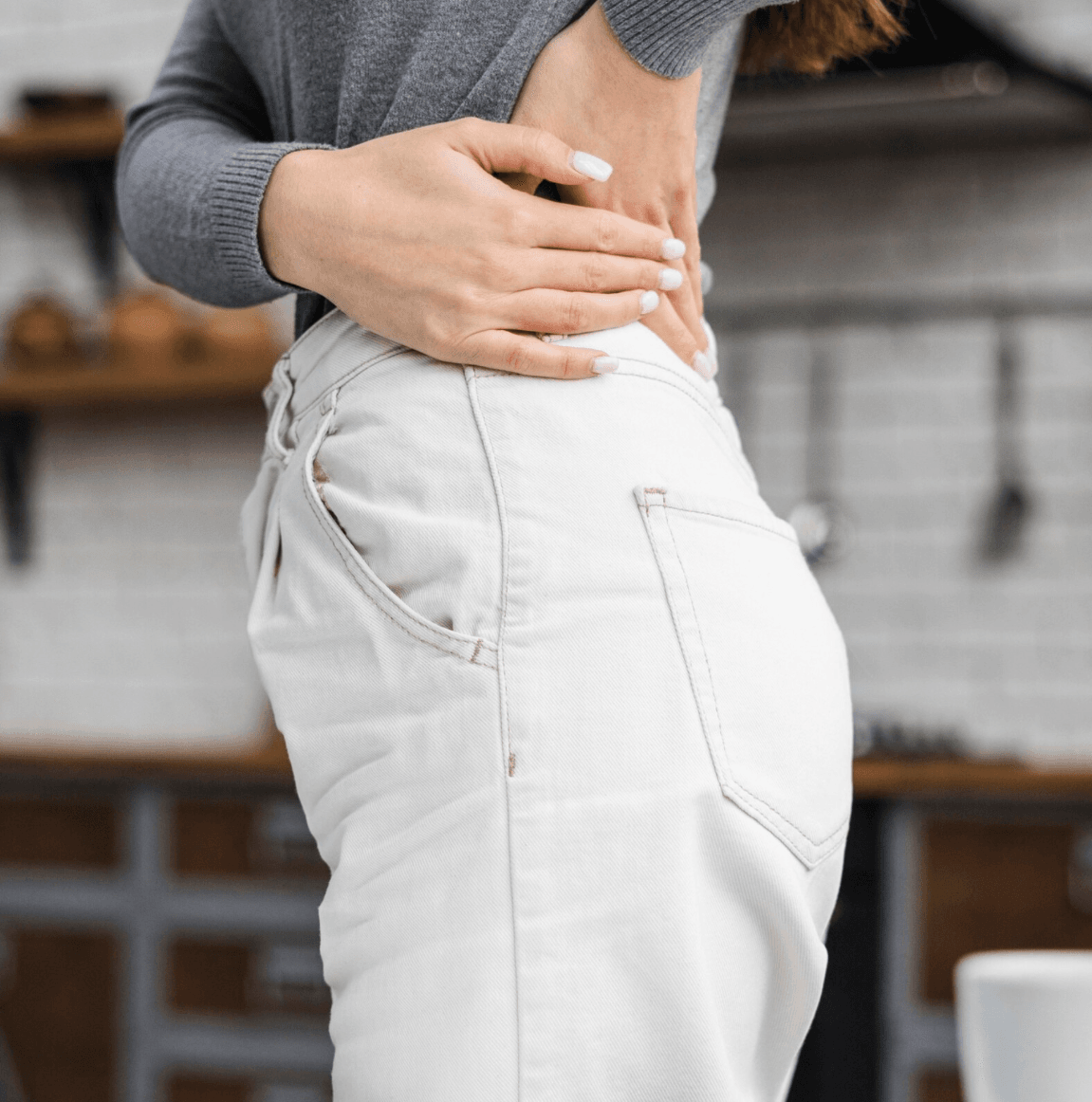 Mulher com dor no nervo ciático tocando região da cintura com as mãos.