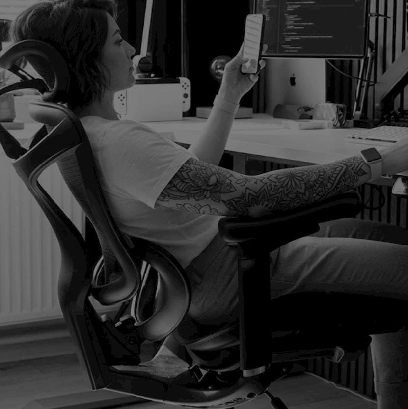 Mulher sentada em cadeira ergonômica no home office, braço tatuado, cadeira ergonômica, cadeira home office, braço todo tatuado